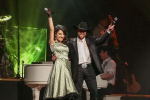 Woman in green dress and man in black jacket and black cowboy hat on stage at Baldknobbers